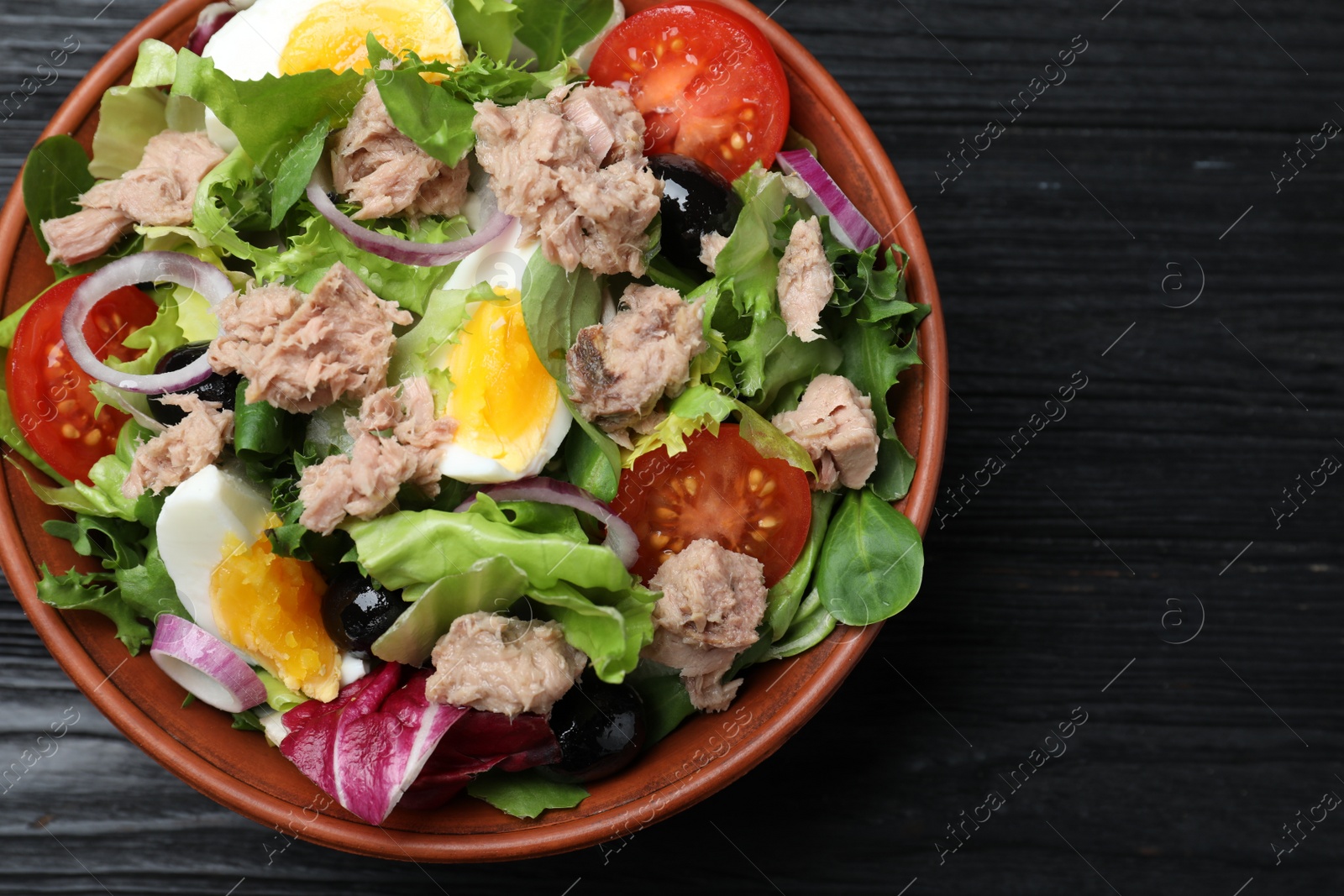 Photo of Bowl of delicious salad with canned tuna and vegetables on black wooden table, top view. Space for text