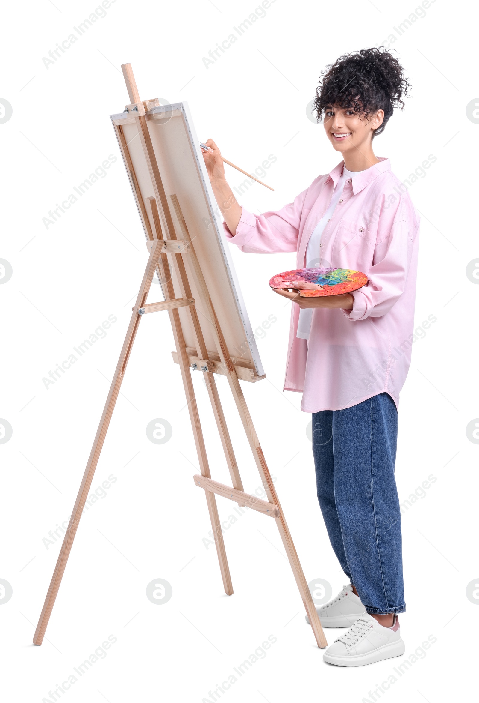 Photo of Young woman painting on easel with canvas against white background