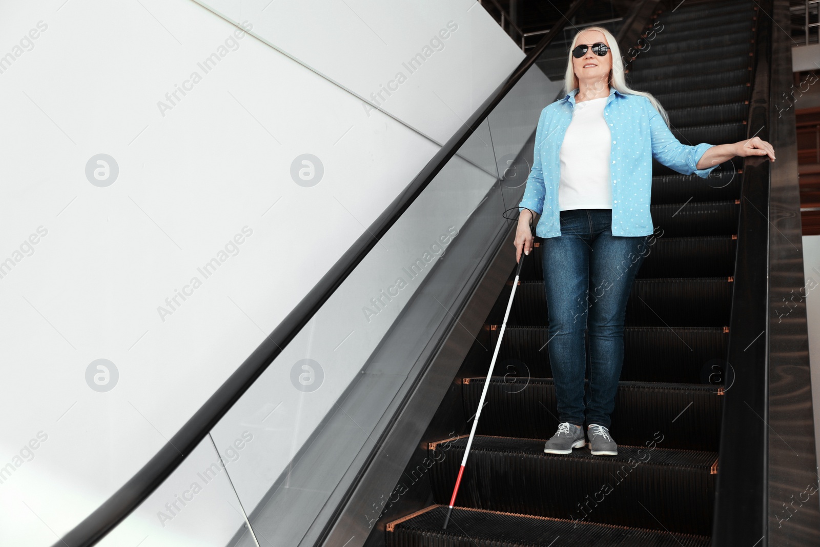 Photo of Blind person with long cane on escalator indoors. Space for text