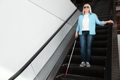 Blind person with long cane on escalator indoors. Space for text