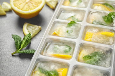 Photo of Ice cubes with lemon and mint in tray on grey table, closeup