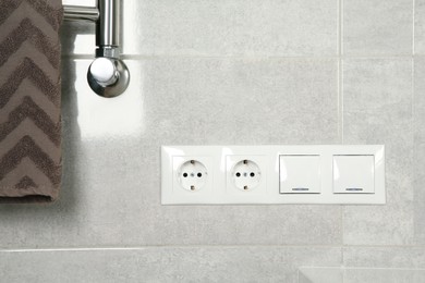 Light switches and power sockets on light grey wall in bathroom