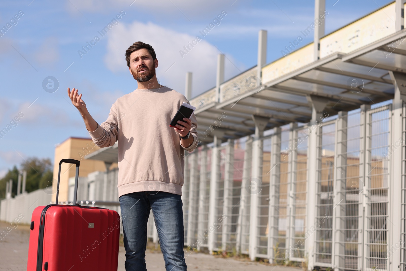 Photo of Being late. Worried man with red suitcase and passport outdoors, space for text