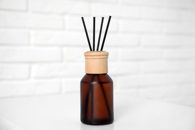 Reed diffuser on table near white brick wall, closeup