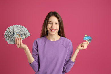 Happy young woman with cash money and credit card on pink background