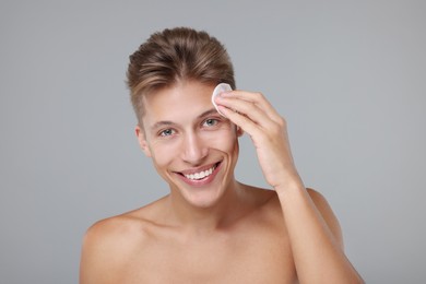 Handsome man cleaning face with cotton pad on grey background