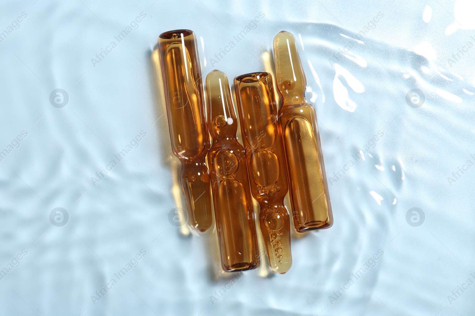 Photo of Skincare ampoules in water on light blue background, top view