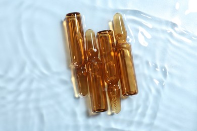 Photo of Skincare ampoules in water on light blue background, top view