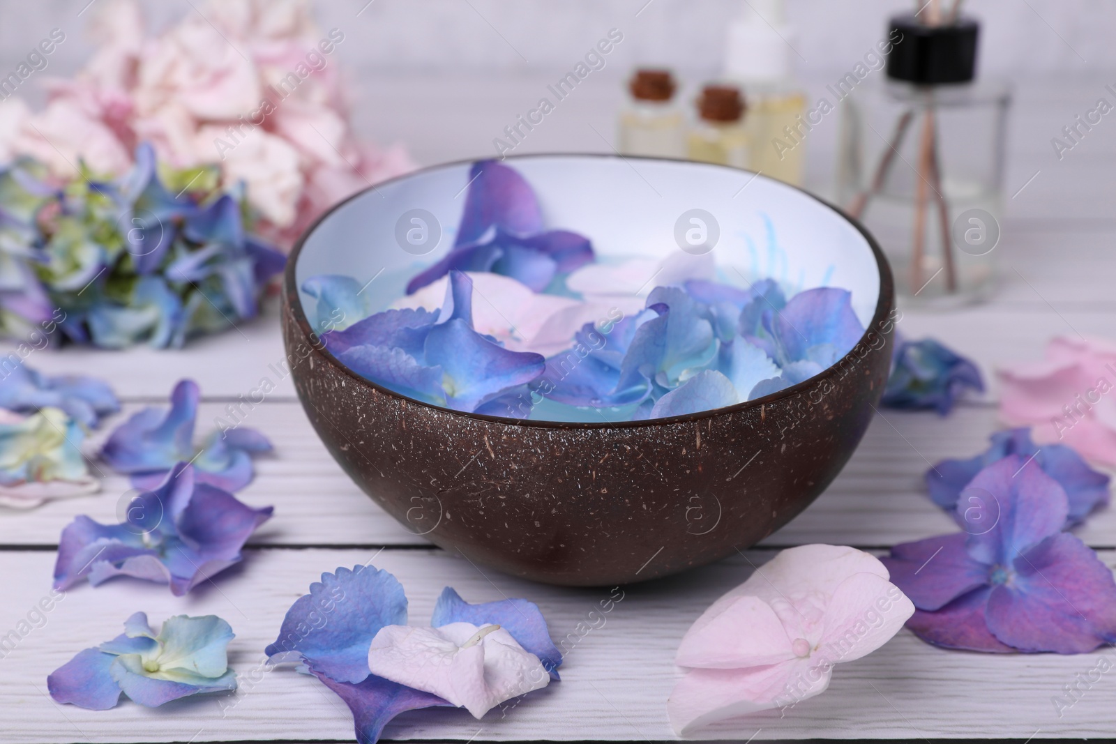 Photo of Spa composition. Aromatic water in bowl and flowers on white wooden table, closeup