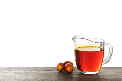 Palm oil in glass jug and fruits on wooden table against white background