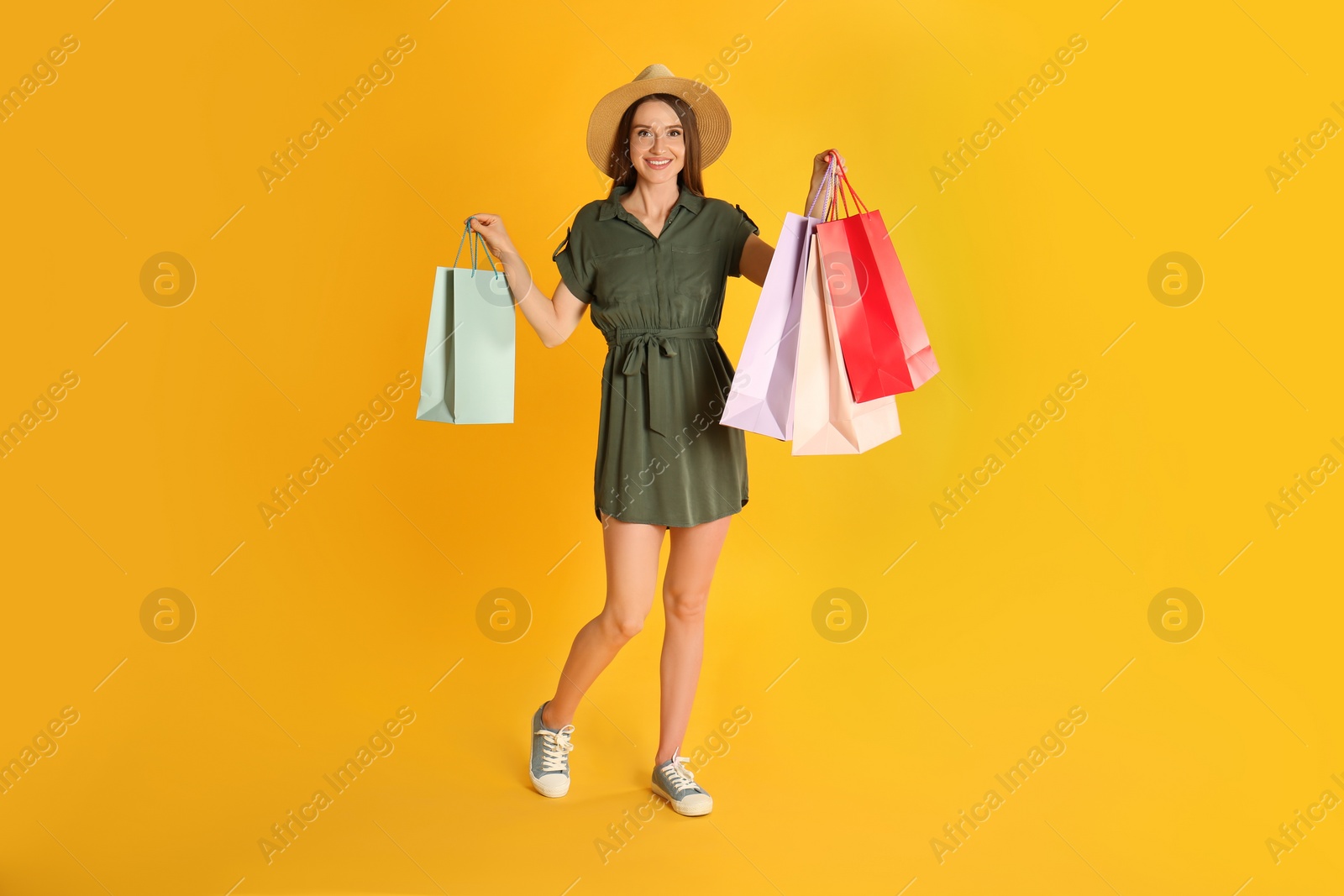 Photo of Beautiful young woman with paper shopping bags on yellow background