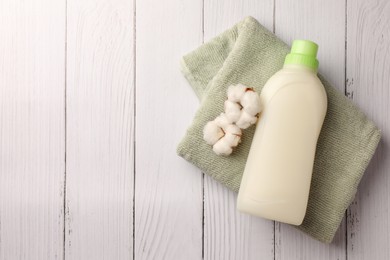 Photo of Bottle of fabric softener, terry towel and beautiful cotton flowers on white wooden surface, top view. Space for text