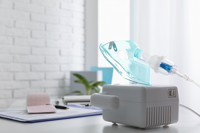 Photo of Modern nebulizer with face mask on white table indoors, space for text. Inhalation equipment