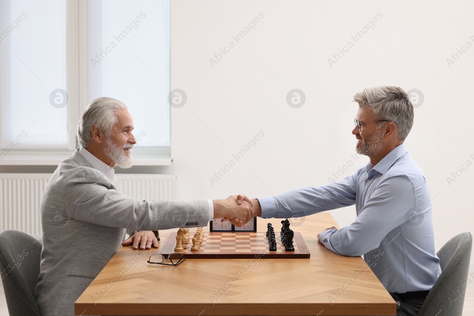 Photo of Men shaking their hands during chess tournament at table indoors