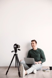Photo of Young blogger with laptop recording video near light wall
