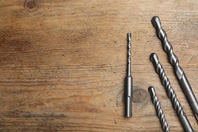 Different drill bits on wooden table, flat lay. Space for text