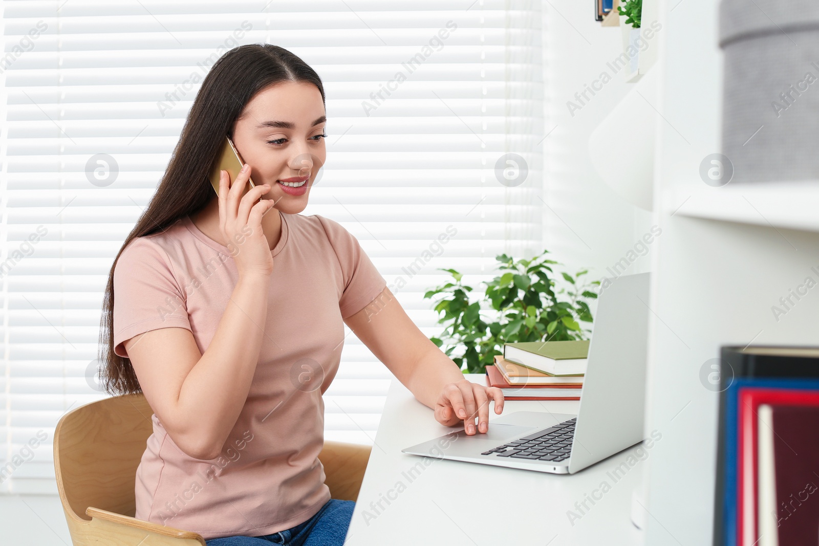 Photo of Home workplace. Happy woman talking on smartphone at white desk in room