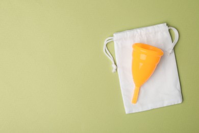 Menstrual cup with bag on light green background, top view. Space for text