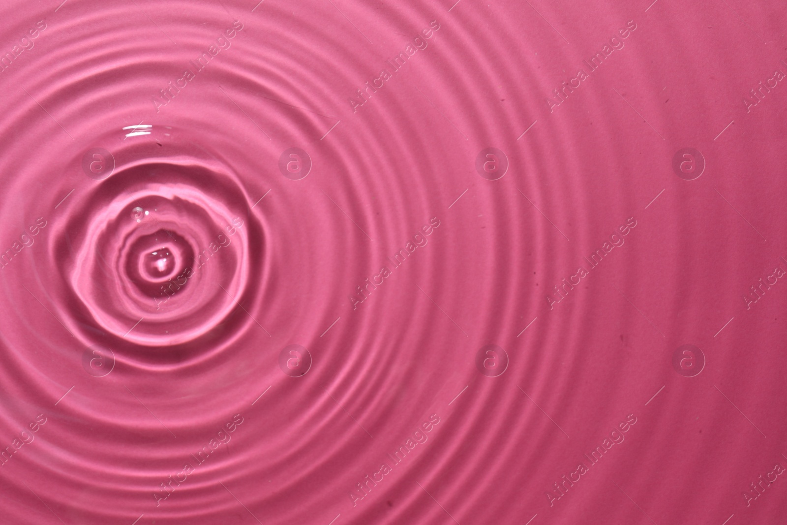 Photo of Rippled surface of clear water on bright pink background, top view