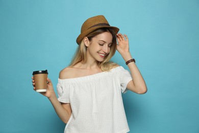 Photo of Beautiful young woman with straw hat and coffee on light blue background. Stylish headdress