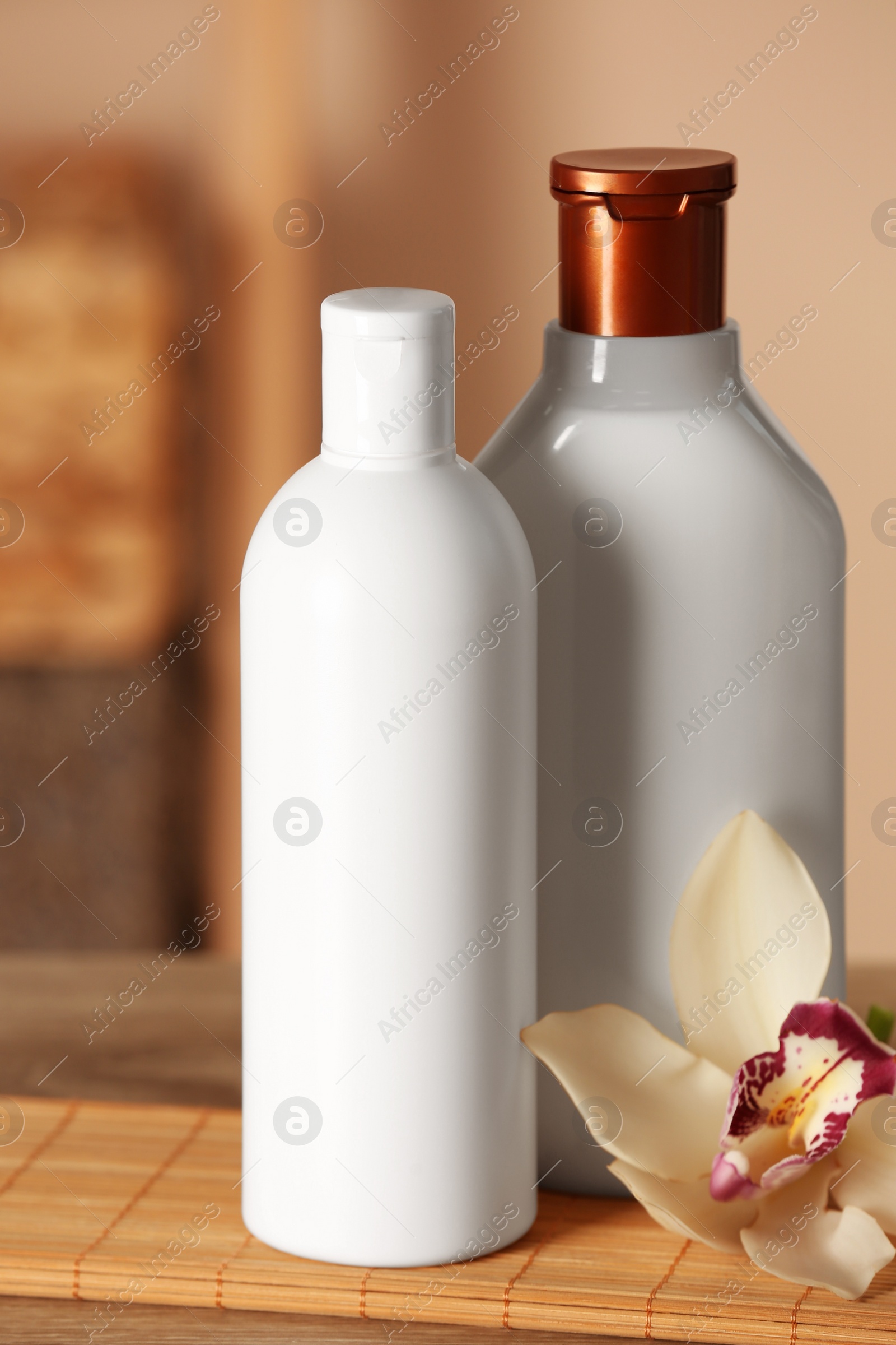 Photo of Bottles of shampoo and flower on wooden table in bathroom