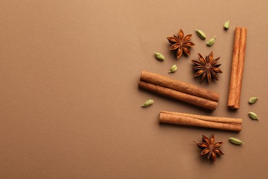 Photo of Cinnamon sticks, star anise and cardamom pods on brown background, flat lay. Space for text