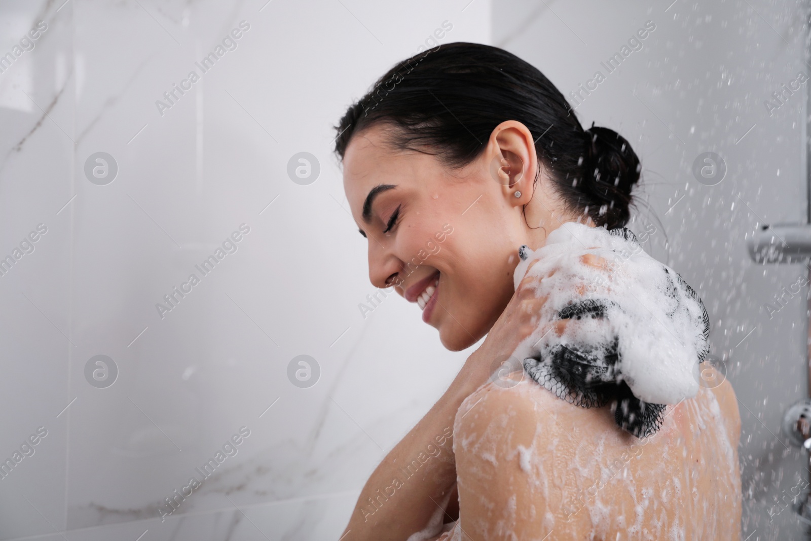 Photo of Young woman with mesh pouf taking shower at home. Space for text