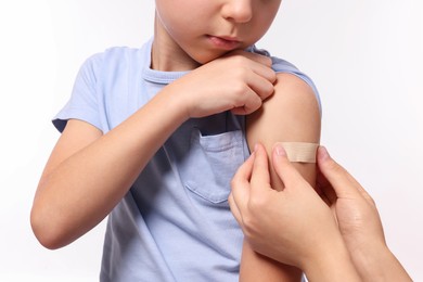 Photo of Woman sticking plaster on boy's arm after vaccination against white background, closeup