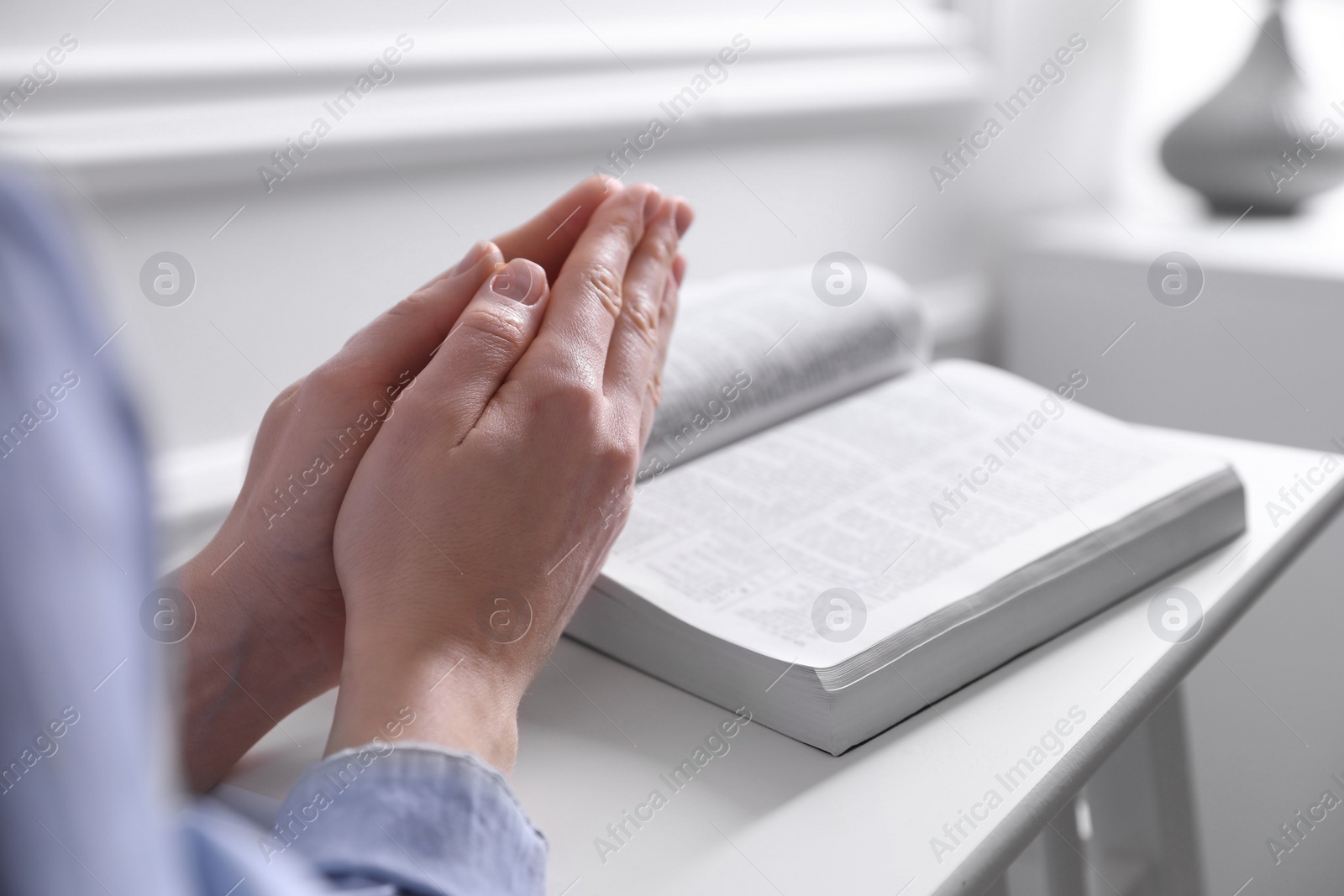 Photo of Religion. Christian woman praying over Bible indoors, closeup