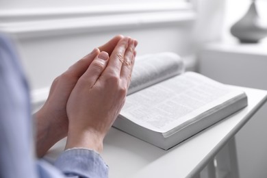 Religion. Christian woman praying over Bible indoors, closeup