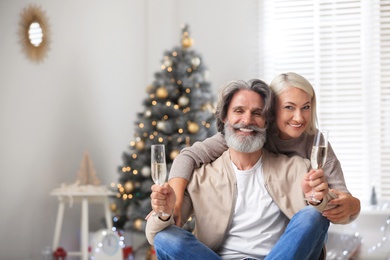 Happy mature couple with glasses of champagne celebrating Christmas at home