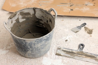 Photo of Bucket with adhesive mix and spatulas on floor indoors