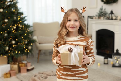 Photo of Happy little girl holding Christmas gift at home