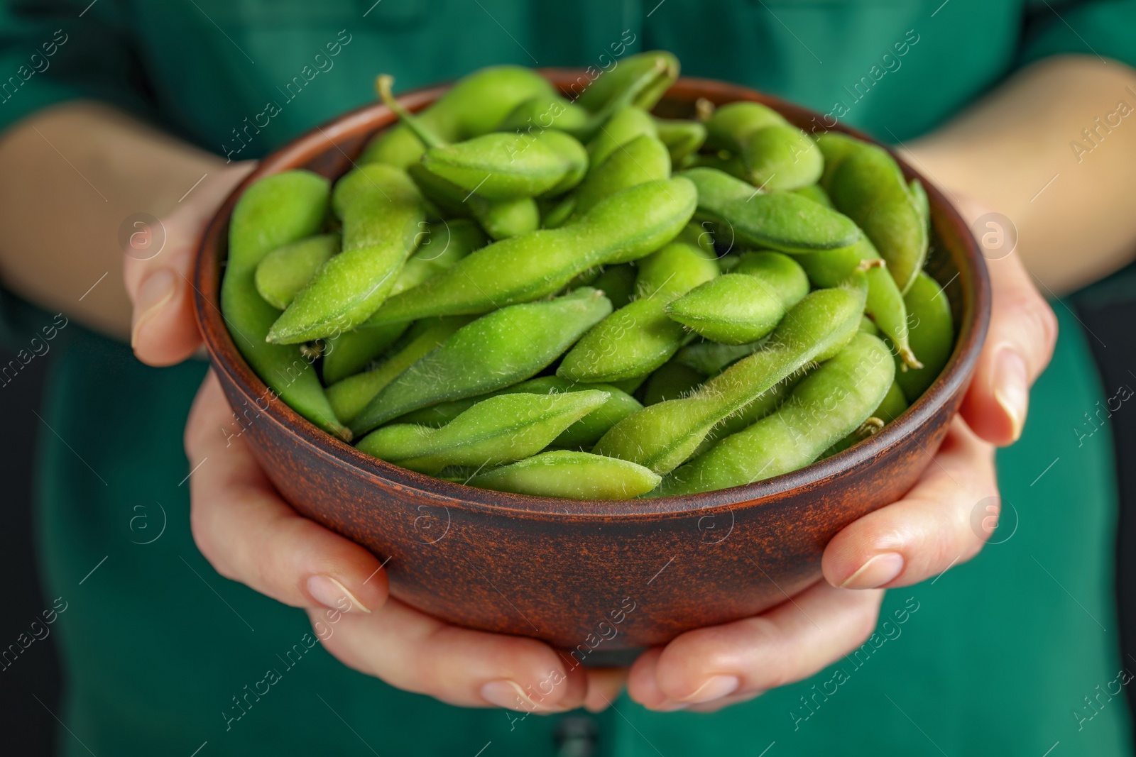 Photo of Woman holding bowl with green edamame beans in pods on black background, closeup