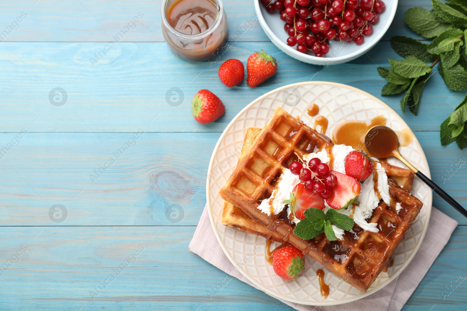Photo of Delicious Belgian waffles with berries and caramel sauce served on turquoise wooden table, flat lay. Space for text