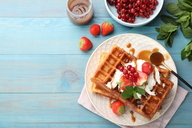 Delicious Belgian waffles with berries and caramel sauce served on turquoise wooden table, flat lay. Space for text