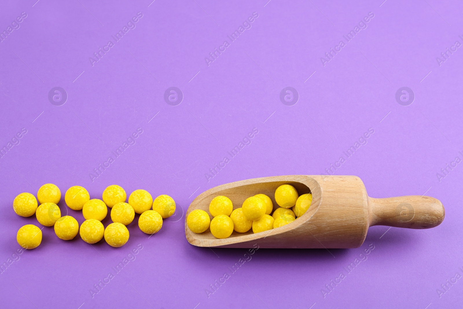 Photo of Delicious lemon chewing gums and scoop on purple background. Space for text