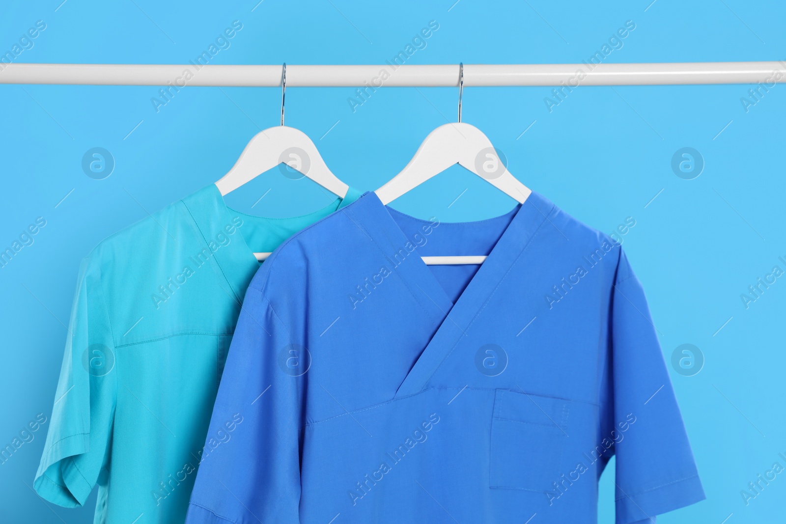 Photo of Medical uniforms on rack against light blue background