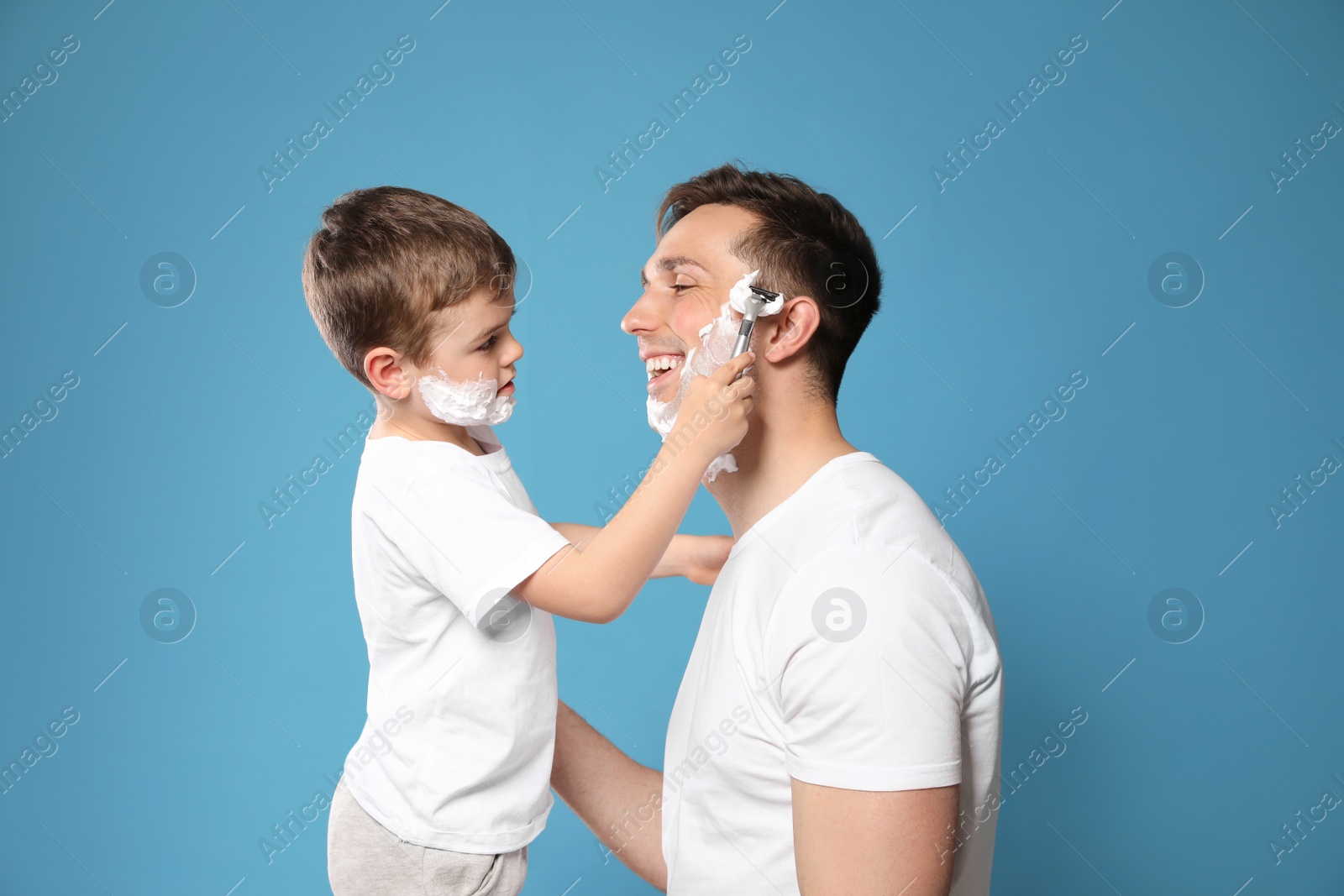 Photo of Little son shaving his dad on color background