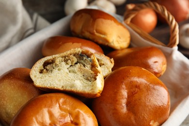Photo of Wicker basket with delicious baked mushrooms and onion pirozhki, closeup