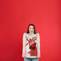 Young woman in Christmas sweater on red background, space for text