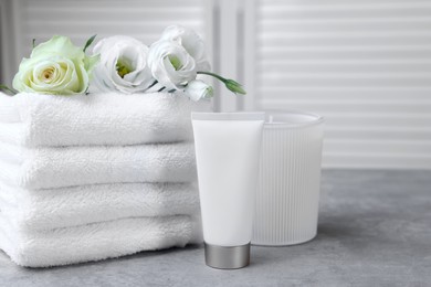 Photo of Towels, tube of lotion, scented candle and flowers on grey table indoors
