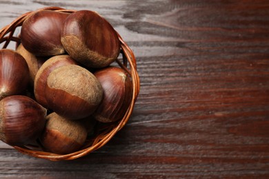 Photo of Sweet fresh edible chestnuts in wicker bowl on wooden table, top view. Space for text