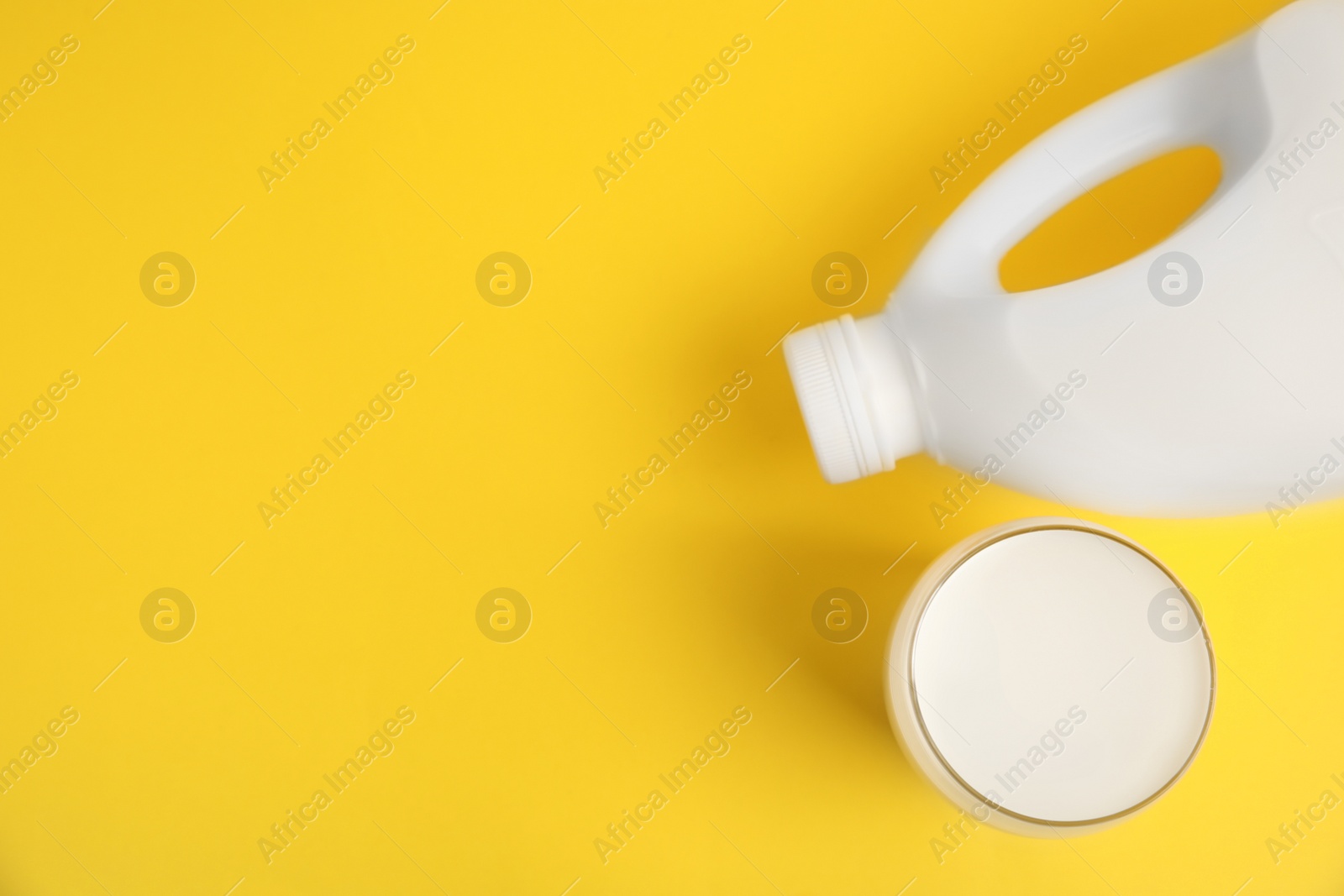 Photo of Gallon bottle and glass of milk on yellow background, flat lay. Space for text