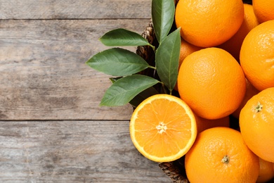 Wicker bowl with ripe oranges on wooden background, top view. Space for text