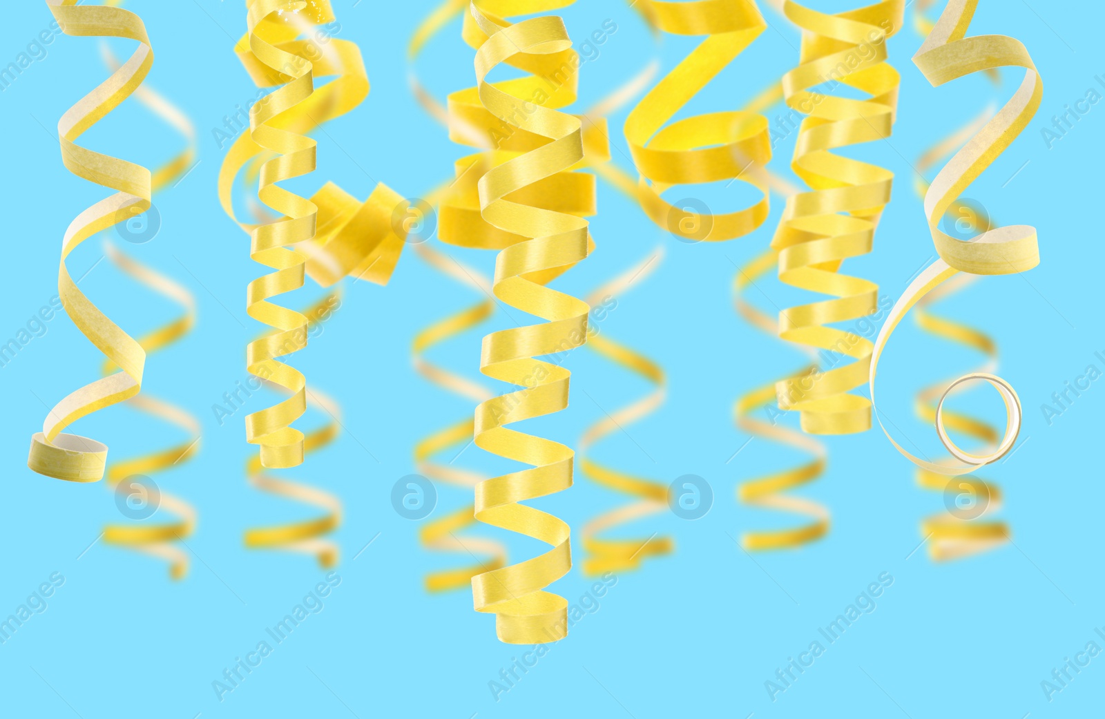 Image of Many yellow serpentine streamers on light blue background. Party decor