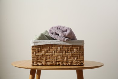 Photo of Clean towels in laundry basket on wooden table against gray background