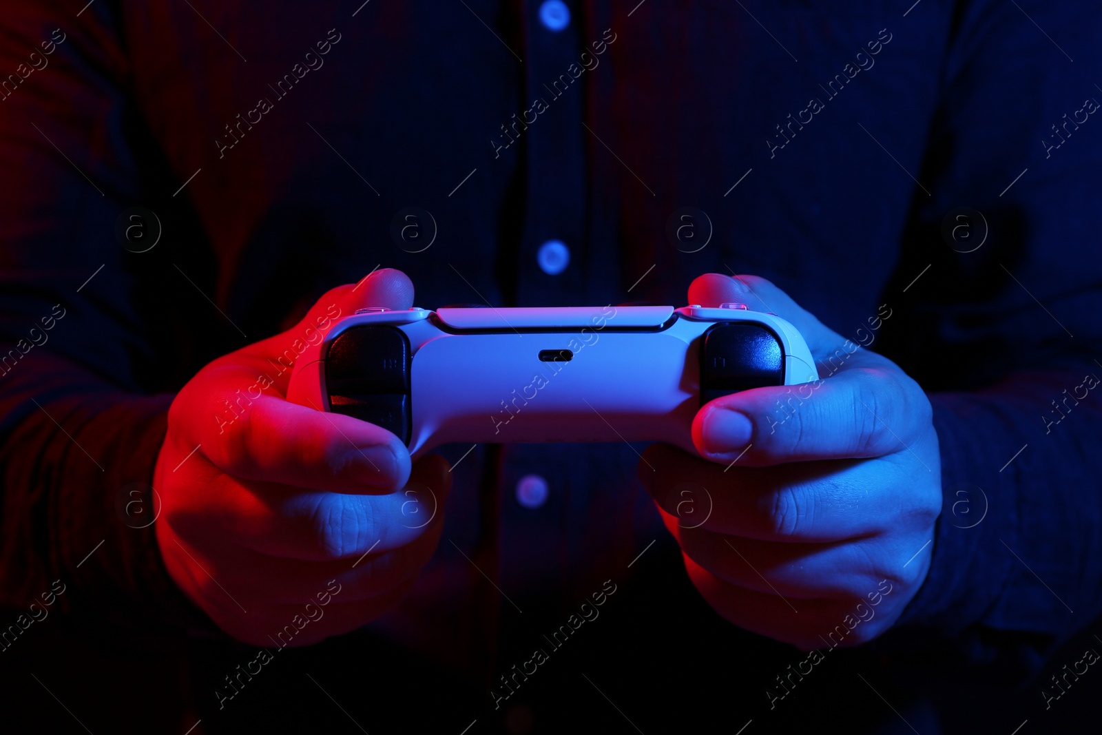 Photo of Man using wireless game controller on dark background in neon lights, closeup