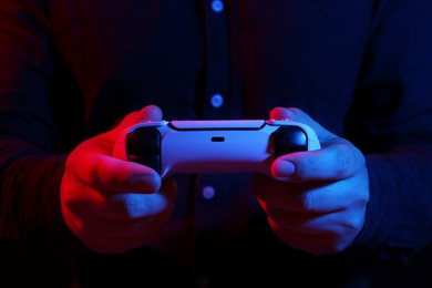 Man using wireless game controller on dark background in neon lights, closeup