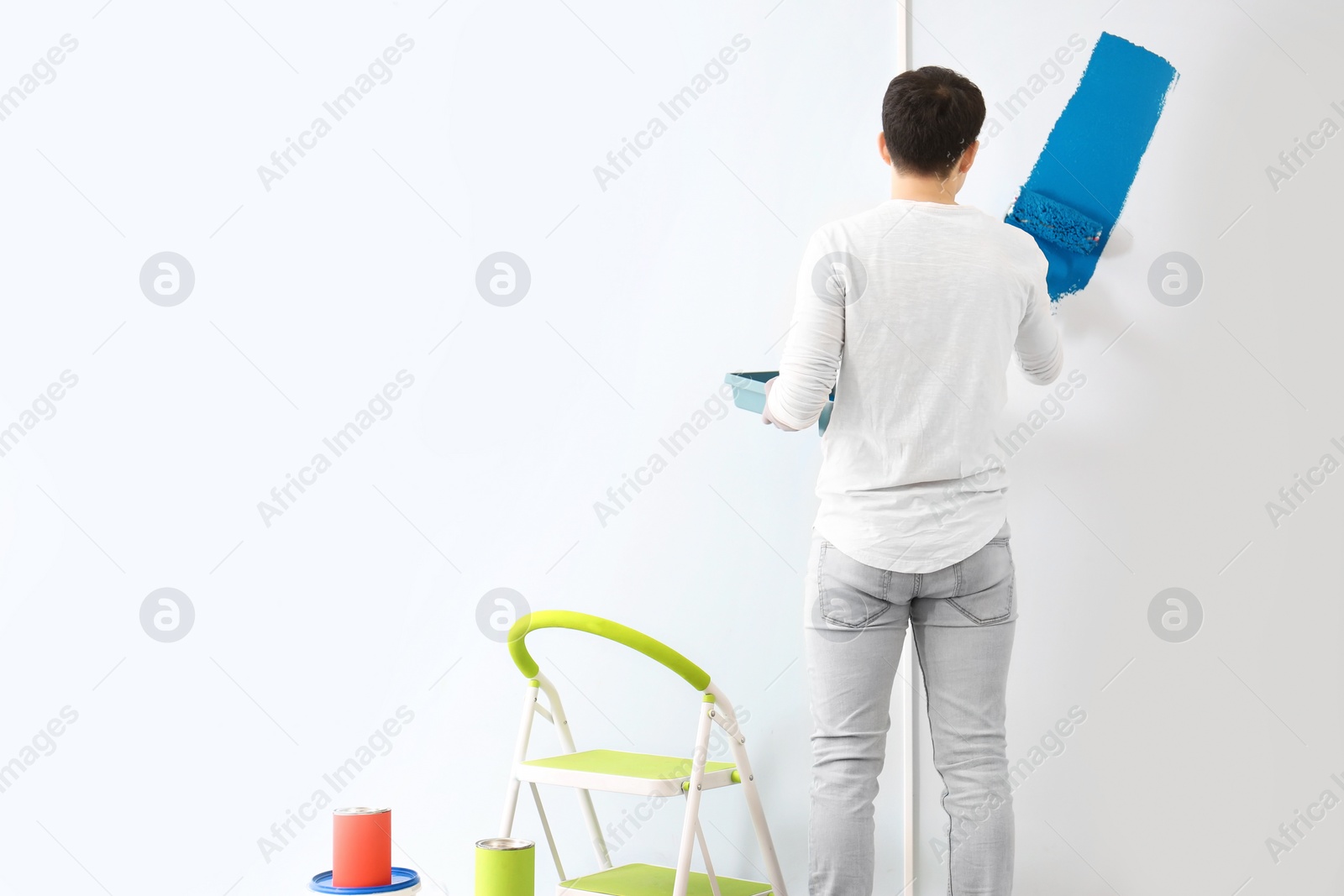 Photo of Male decorator painting wall with roller indoors